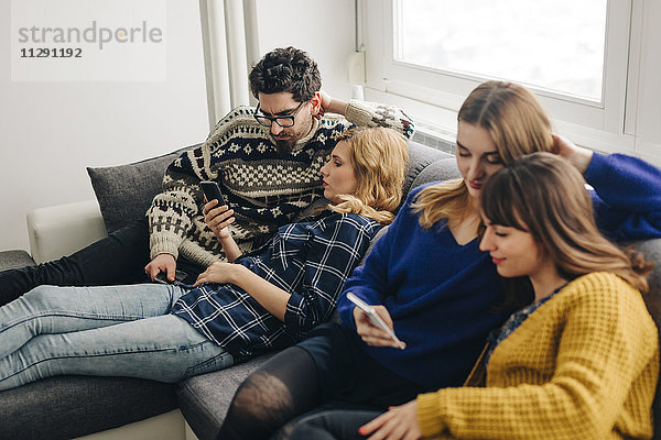 Vier Freunde mit Smartphones auf der Couch im Wohnzimmer hängen heraus