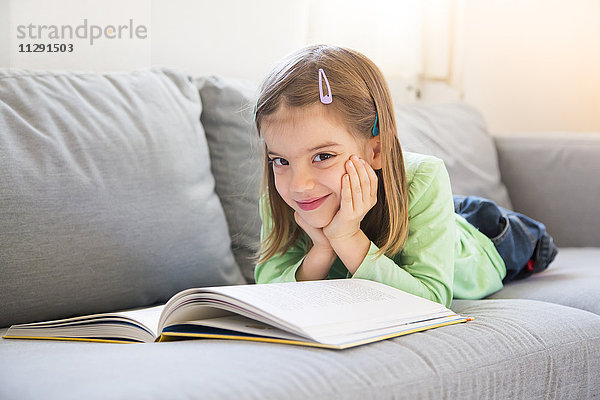 Porträt des lächelnden Mädchens auf der Couch mit Buch