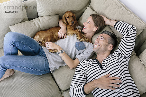 Lächelndes Paar mit Hund auf der Couch liegend
