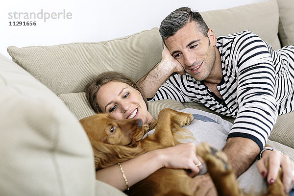 Lächelndes Paar mit Hund auf der Couch liegend