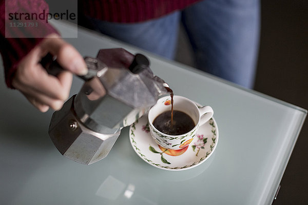 Hand einer jungen Frau  die Kaffee in eine Tasse gießt.