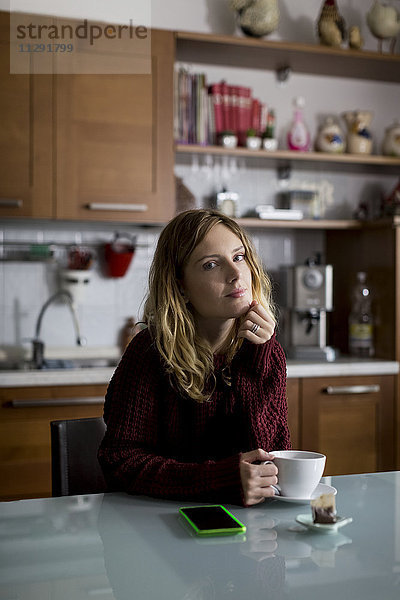 Porträt einer in der Küche sitzenden Frau mit einer Tasse Tee