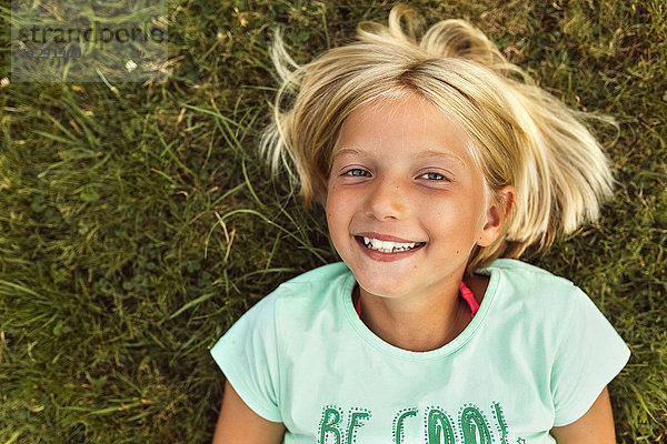 Porträt eines lächelnden blonden Mädchens auf einer Wiese liegend