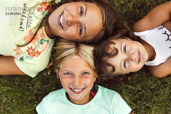 Drei lächelnde Mädchen liegen Kopf an Kopf auf einer Wiese.