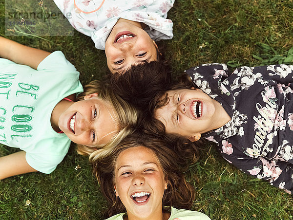 Vier lachende Mädchen liegen Kopf an Kopf auf einer Wiese.