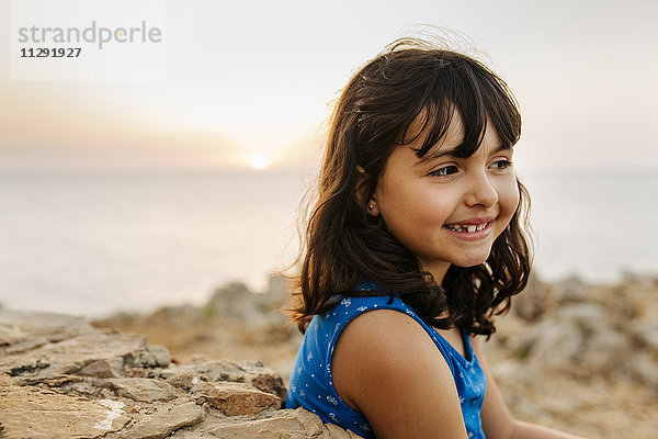 Porträt eines glücklichen kleinen Mädchens am Meer bei Sonnenuntergang