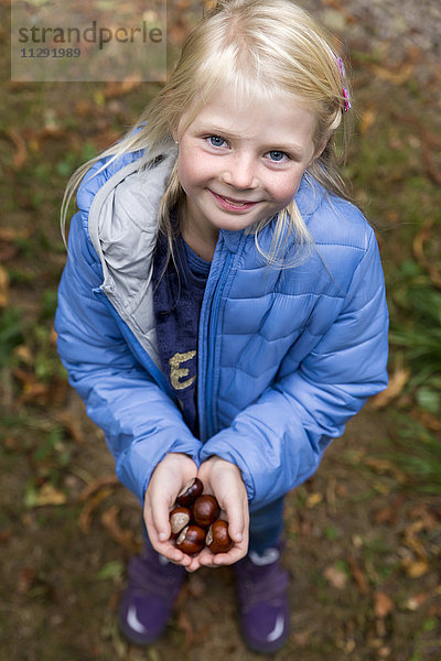 Porträt eines lächelnden blonden Mädchens mit Kastanien in den Händen