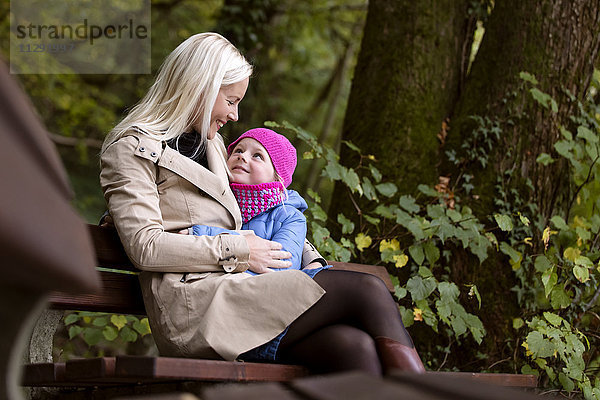 Mutter und kleine Tochter sitzen auf einer Bank im Herbstwald