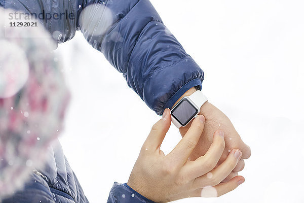 Mann beim Prüfen seiner Smartwatch im Winter  Teilansicht