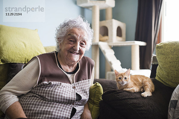 Porträt einer glücklichen Frau und ihrer Katze  die auf der Couch im Wohnzimmer sitzt.