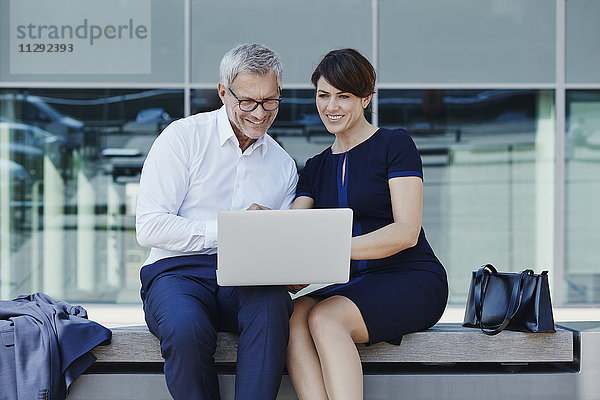 Geschäftsmann und Geschäftsfrau sitzen auf einer Bank und teilen sich einen Laptop.