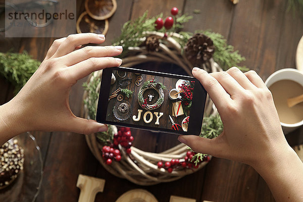 Frauenhände fotografieren selbstgemachten Adventskranz mit Smartphone