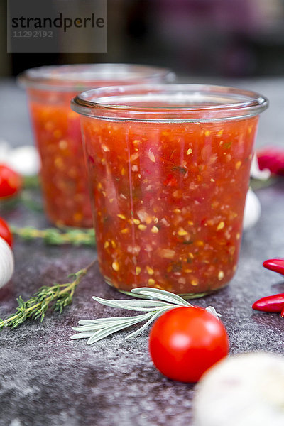 Gläser mit hausgemachter Tomatensauce und Zutaten auf Stein