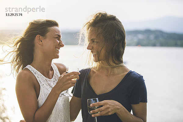 Italien  Gardasee  zwei glückliche junge Frauen am Seeufer bei einem Glas Wein