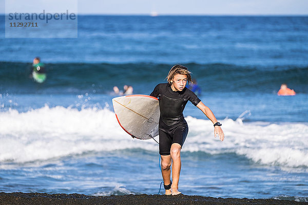 Spanien  Teneriffa  Junge mit Surfbrett am Meer
