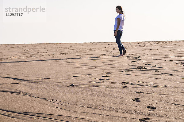 Junge Frau  die im Sand am Strand spazieren geht.