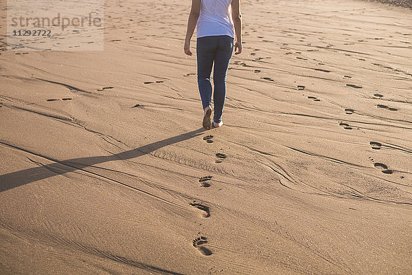 Junge Frau  die im Sand am Strand spazieren geht.