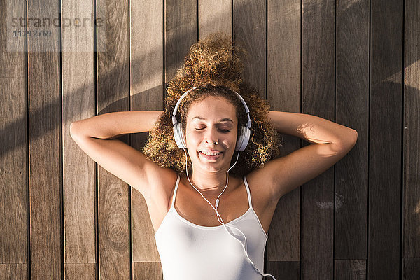 Porträt einer jungen Frau mit geschlossenen Augen auf Holzboden liegend  Musik hören mit Kopfhörer