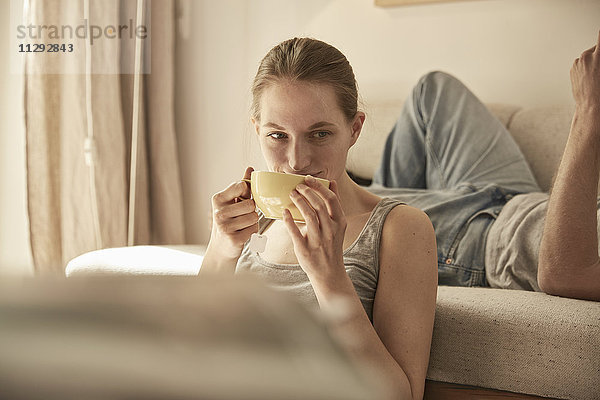 Frau trinkt Tee im Wohnzimmer mit Mann im Hintergrund