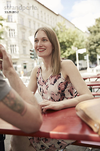 Lächelnde Frau  die den Mann in einem Straßencafé ansieht.