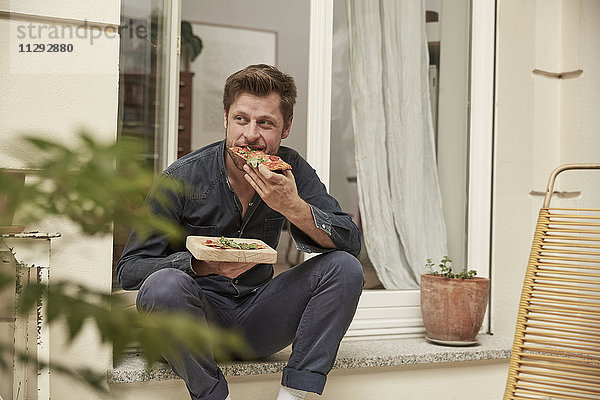 Mann isst Pizza vor der Haustür