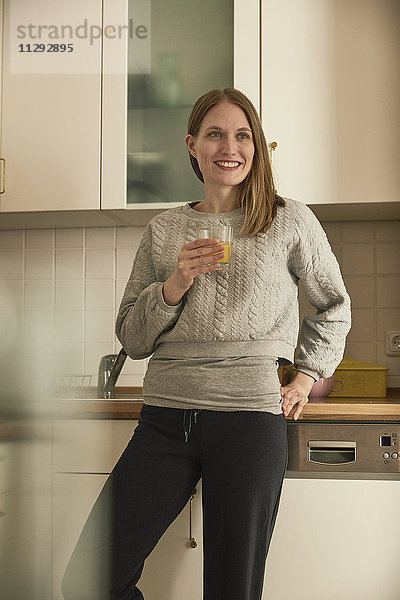 Lächelnde Frau trinkt Saft in der Küche