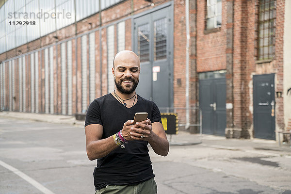 Porträt eines lächelnden Mannes  der sein Handy ansieht.