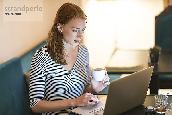 Porträt einer Frau  die in einem Café sitzt und einen Laptop benutzt.