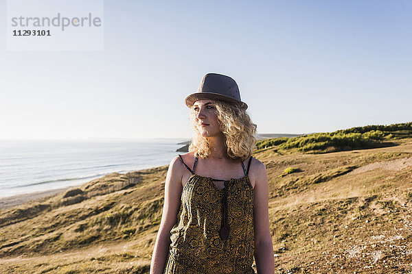 Blondes Teenagermädchen mit Hut am Meer in der Abenddämmerung