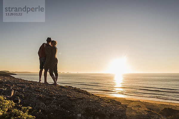 Rückansicht des verliebten jungen Paares bei Sonnenuntergang am Meer