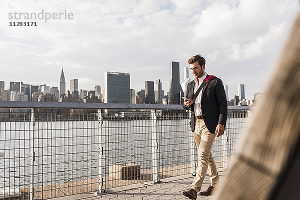 USA  New York City  Geschäftsmann  der am East River entlang läuft und sich das Handy ansieht.