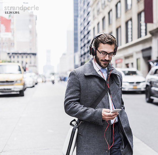 USA  New York City  Geschäftsmann mit Handy und Kopfhörer unterwegs