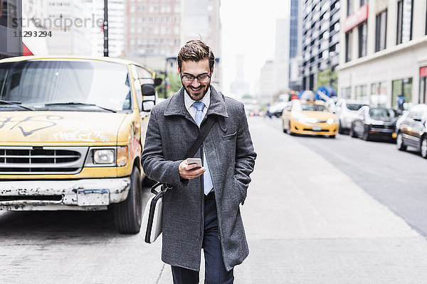 USA  New York City  lächelnder Geschäftsmann mit Handy unterwegs