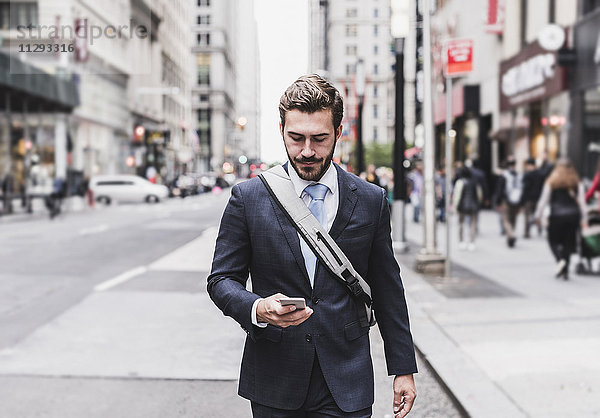 USA  New York City  Geschäftsmann  der in Manhattan spazieren geht und sich das Handy ansieht.