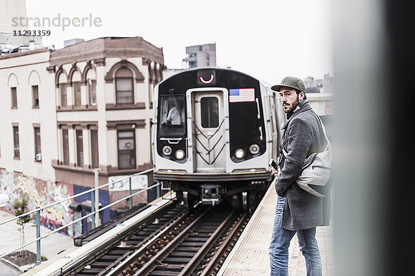 Junger Mann wartet auf die U-Bahn am Bahnsteig  hält Smartphone