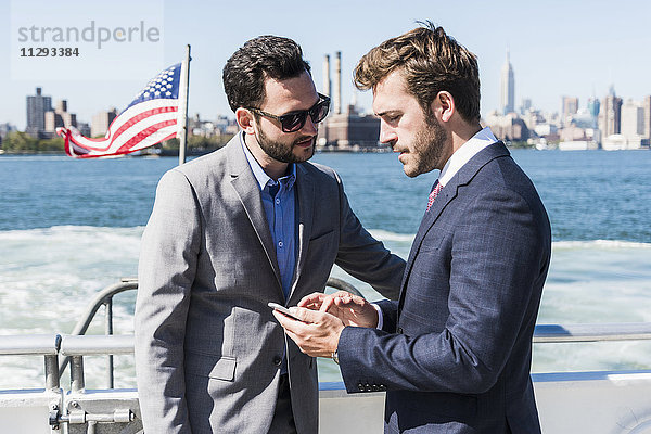 USA  New York City  zwei Geschäftsleute mit Handy auf der Fähre auf East River