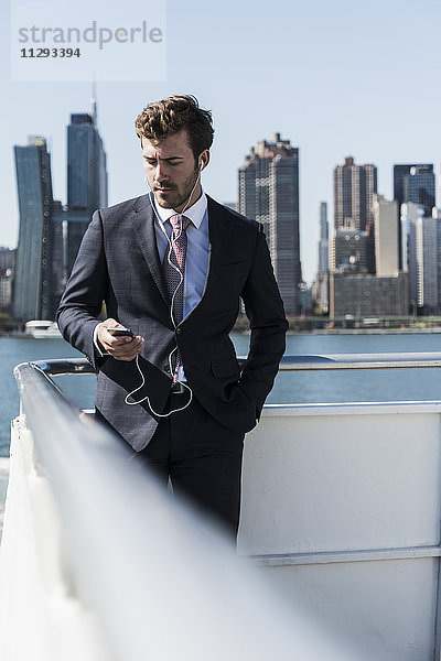 USA  New York City  Geschäftsmann auf der Fähre auf dem East River mit Handy und Kopfhörer