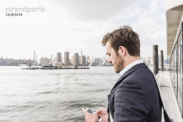 USA  New York City  Geschäftsmann auf der Fähre auf dem East River  der sein Handy überprüft.