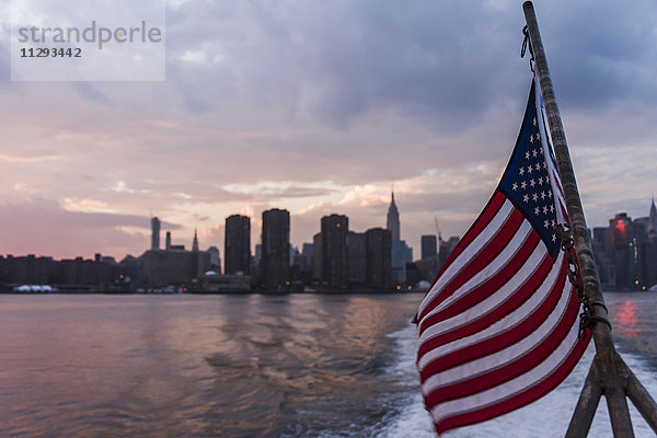 USA  New York City  US-Flagge auf der Fähre am East River mit Skyline von Manhattan im Hintergrund