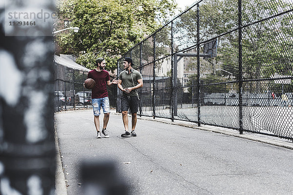 Zwei Freunde  die mit Basketball im Freien spazieren gehen.