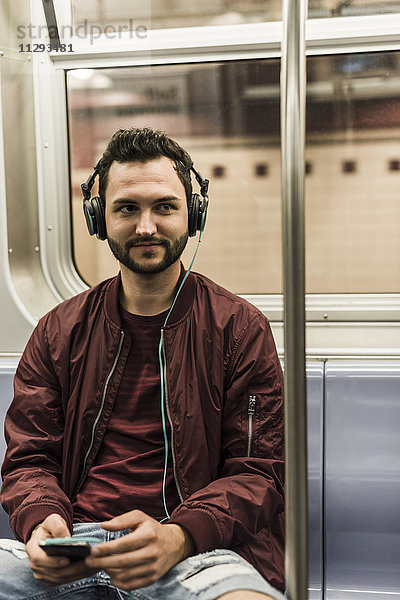 Junger Mann sitzt in der U-Bahn und trägt Kopfhörer.