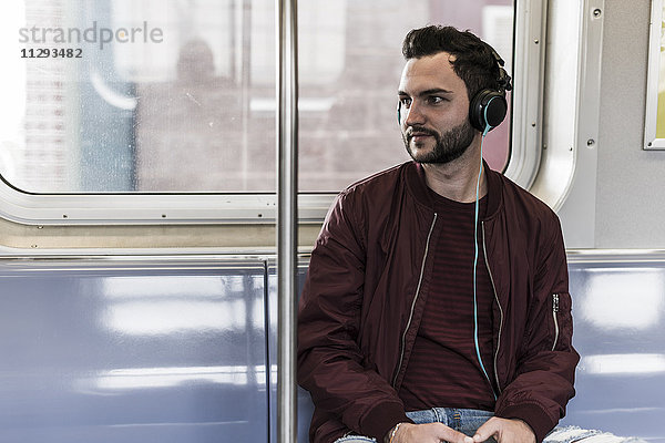 Junger Mann sitzt in der U-Bahn und trägt Kopfhörer.
