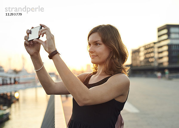 Deutschland  Junge Frau in Hamburg fotografiert mit ihrem Smartphone