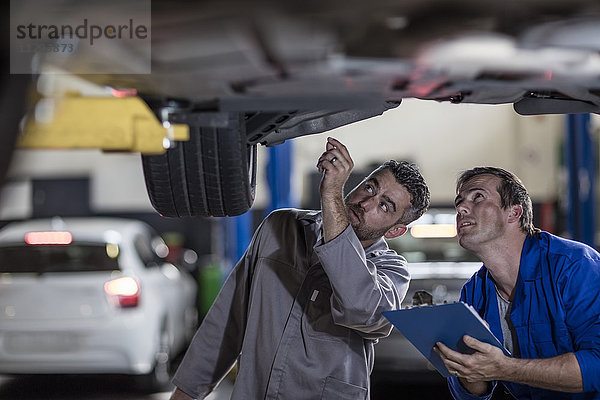 Zwei Kfz-Mechaniker in einer Werkstatt  die das Auto gemeinsam untersuchen.