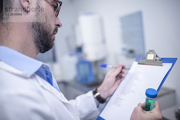 Wissenschaftlerin mit Zwischenablage und Reagenzglas im Labor