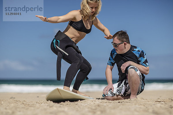 Jugendlicher Junge mit Down-Syndrom beim Surfunterricht am Strand