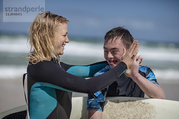Glücklicher Teenager mit Down-Syndrom und Frau mit Surfbrett am Strand