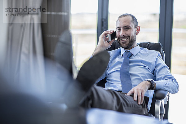 Lächelnder Geschäftsmann sitzt an seinem Schreibtisch und telefoniert.