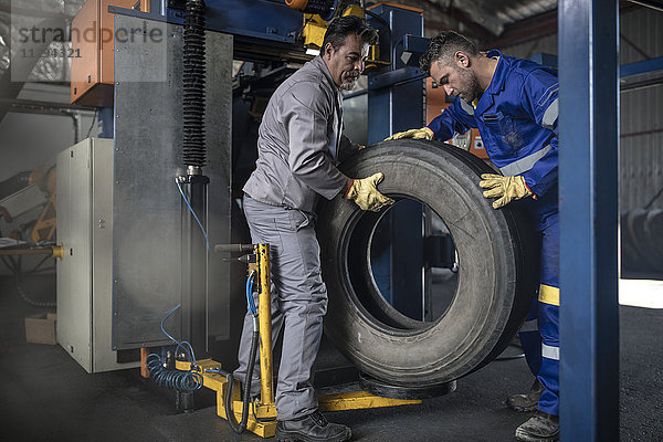 Zwei Reifenmonteure heben Reifen in der Fabrik