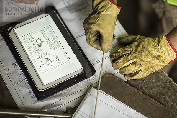 Mann im Bauunternehmen arbeitet mit Blaupause auf digitalem Tablett
